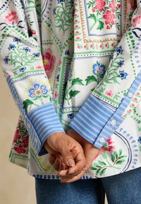 Floral-patterned shirt made of cotton, featuring a white base, colorful floral designs, and a light blue striped cuff with buttons.