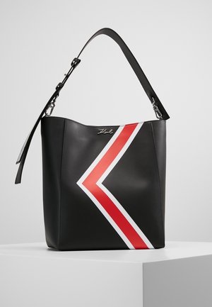 Black handbag with adjustable strap, red and white chevron stripe, and silver brand logo on front, placed on white surface.