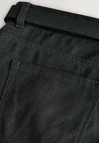 Juodos austos medžiagos kelnės, turinčios tekstūruotą, tvirtą diržo sritį su matomomis siūlėmis ir didelį užpakalinį kišenę.