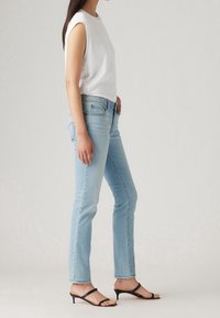 Top blanco sin mangas, vaqueros rectos de color azul claro y sandalias de tacón negro con tiras. La tela parece suave con detalles de diseño mínimos.