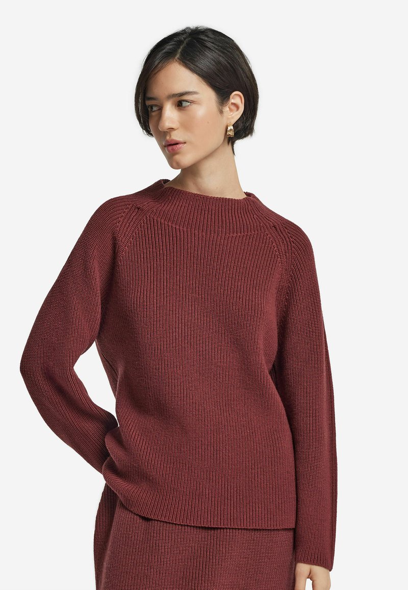 Burgundy stickad tröja med hög hals, ribbad textur och långa ärmar. Har en avslappnad passform och subtila sömdetaljer.