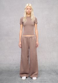 Camiseta corta marrón de manga corta combinada con pantalones de chándal marrones de corte holgado, con cintura elástica y bolsillos laterales.