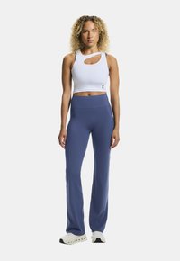 Biały sportowy crop top z wycięciem, zestawiony z niebieskimi spodniami o wysokim stanie, noszony w białych sneakersach. Dopasowany krój, gładka tekstura.