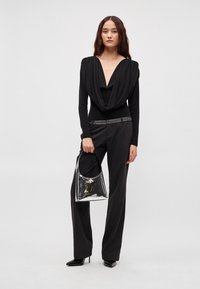 Czarna, długorękawowa bluzka z głębokim dekoltem w kształcie litery V, zestawiona z ciemnymi spodniami z nitowanym paskiem i błyszczącą srebrną torebką.