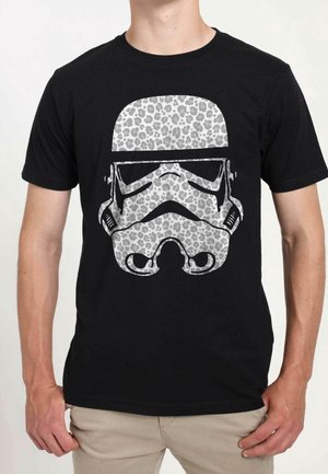 Person trägt ein schwarzes T-Shirt mit einer weißen Stormtrooper-Helm-Grafik und einem grauen Leopardenmuster.