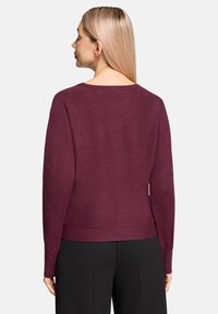 Bordeauxrode trui met lange mouwen en een ontspannen pasvorm, voorzien van een ronde halslijn en geribbelde zoom. Gladde, gestructureerde stof.