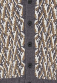 Gros plan d'un cardigan gris avec des boutons noirs et un motif tricoté en blanc, beige et gris foncé.