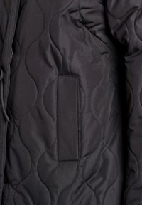 Čierna prešívaná bunda s vlnitou textúrou, náprsným vreckom a sťahovacou šnúrkou na úpravu. Materiál pôsobí hladko a ľahko.