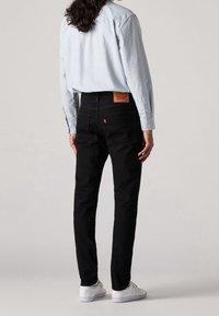 Svarta jeans i denim med rak skärning och bakfickor. Kombinerade med en ljusblå randig långärmad skjorta och vita sneakers.