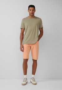 Khaki bawełniana koszulka połączona z brzoskwiniowymi dżinsowymi szortami w standardowym kroju. Obuwie to kremowe sneakersy z jasnobrązowymi akcentami.