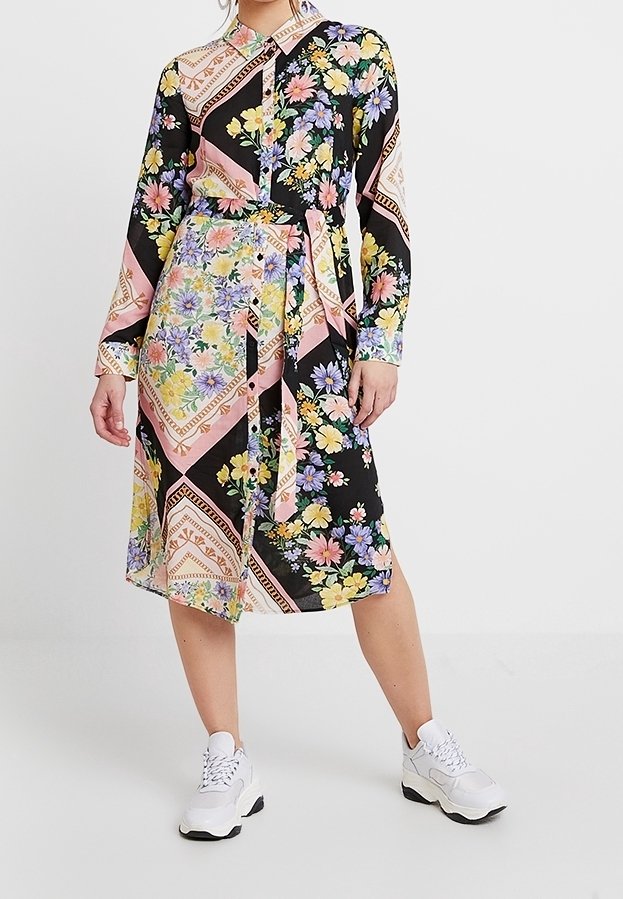 Robe mi-longue florale avec une base noire ornée de motifs floraux roses et jaunes, une taille ceinturée et un col boutonné.
