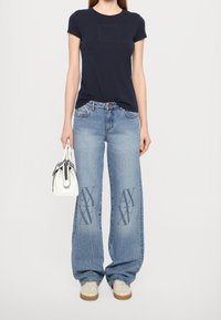 Námořnická trička s krátkým rukávem s logem, světle modré široké džíny s ornamentálními detaily a malá bílá kabelka. Celkový vzhled doplňují béžové tenisky.