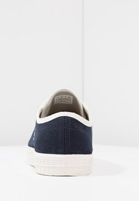 Navy canvas sneaker with a white rubber sole, featuring a rounded back, contrasting stitching, and a smooth finish on the outer material.