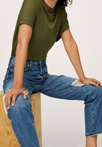 Oliwkowa bluzka z krótkim rękawem i prążkowanym dekoltem, zestawiona z niebieskimi dżinsami z wysokim stanem, które mają przetarcia i luźny krój.