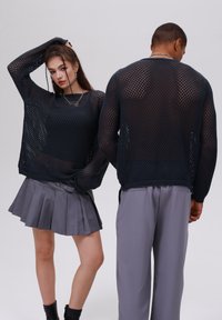 Maglione a maglia a rete color navale con maniche lunghe e polsini a coste, indossato con una gonna plissettata grigia e pantaloni, entrambi in tessuto texturizzato.