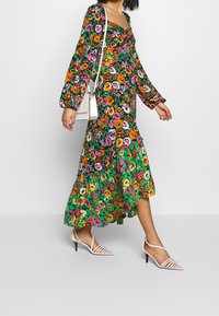 Abito midi floreale con sfondo nero, fiori multicolori vivaci, maniche lunghe a sbuffo e orlo arricciato. Abbinato a tacchi bianchi con cinturini.