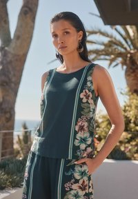 Ärmelloses Top in Teal mit floralem Muster und vertikalen Streifen, mit Hibiskusblüten und Blättern an den Seiten; lockere Passform; leichtes Material.