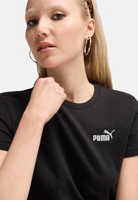 Sort bomulds T-shirt med rund halsudskæring og korte ærmer, med et hvidt Puma-logo på venstre brystområde. Glat tekstur.