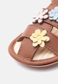 Καφέ δερμάτινο σανδάλι με ανοιχτό νύχι και διακοσμητικά λουλούδια σε παστέλ ροζ, μπλε και κίτρινες αποχρώσεις στα λουριά.