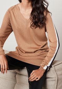 Brauner V-Ausschnitt-Pullover mit langen Ärmeln, der weiße und schwarze Streifen an den Ärmeln hat, eine gerippte Textur aufweist und eine lockere Passform bietet.