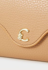 Beige leren handtas met een gestructureerde afwerking. Voorzien van een goudkleurig C-vormig logo en golvende stikseldetails langs de bovenrand.