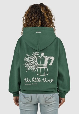 Person with curly hair faces away wearing green hoodie with moka pot, flowers, and text "the little things Moments to Memories" on back.