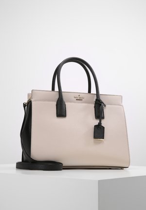 Beige en zwarte gestructureerde handtas met twee handvatten, een schouderriem en een hangend label, geplaatst op een wit oppervlak tegen een effen achtergrond.