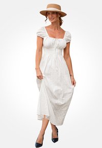 Vestido maxi blanco texturizado con mangas abullonadas y escote cuadrado. Presenta una cintura ajustada y sutiles rayas verticales, combinado con tacones negros.