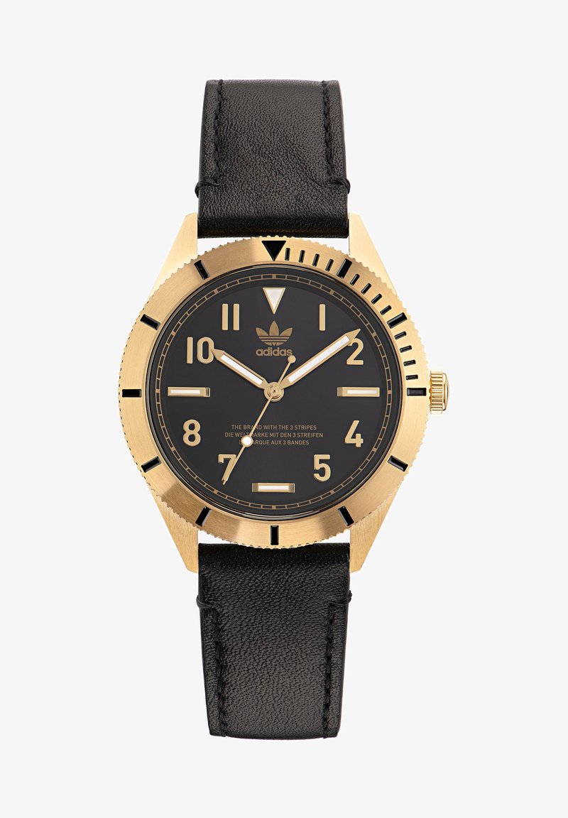 Kuldset tooni kell musta dialiga, suurte helendavate tunni märkidega, musta nahkrihmaga ja hambulise äärisega. Omab Adidas'i logo.