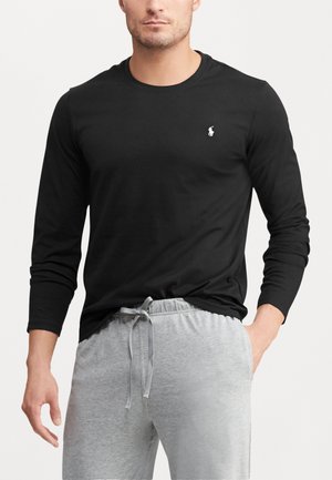 Zwarte longsleeve t-shirt met een wit logo, gecombineerd met grijze sweatpants met een trekkoord. Glad stoftextuur, casual pasvorm.