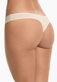 Beige slip met een gladde textuur en een minimalistisch ontwerp. Heeft een zachte tailleband en een lage snit, wat zorgt voor een naadloze uitstraling.