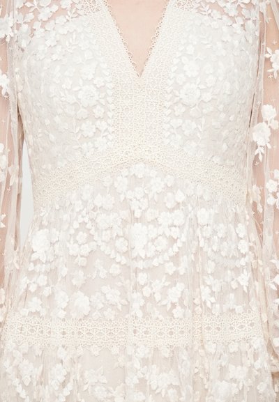 Rochie albă din dantelă, cu broderii florale, decolteu în V și mâneci lungi din material transparent. Corpul rochiei are un model texturat din dantelă, cu o bandă orizontală din dantelă.