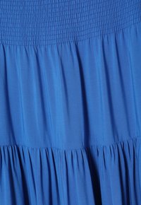 Abito blu con corpetto arricciato e gonna a pieghe svasata. Il tessuto è morbido e setoso, creando una silhouette fluida.