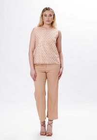 Top senza maniche rosa chiaro con un motivo esagonale testurizzato, abbinato a pantaloni beige larghi e tacchi nudi con cinturini.