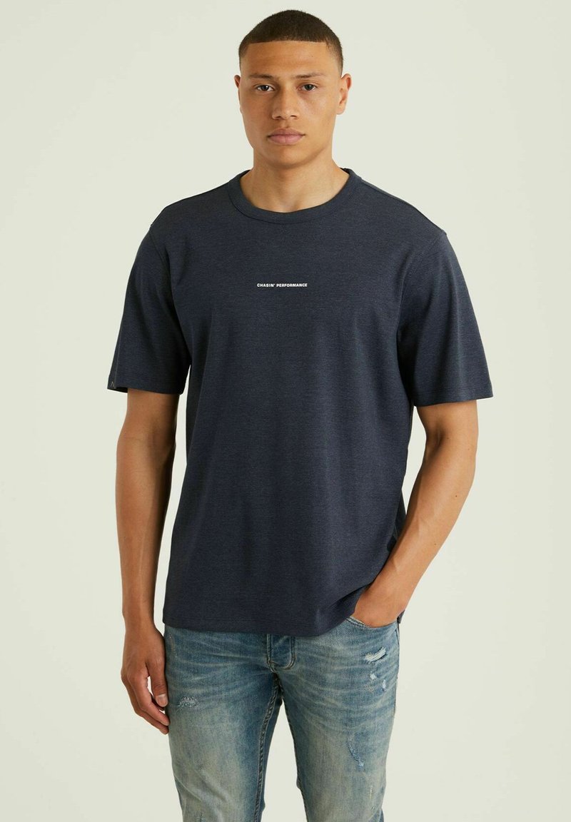 T-paita, jossa on lyhyet hihat ja pyöreä kaula-aukko, tummansinisessä värissä. Edessä valkoinen logo-teksti "CHASIN' PERFORMANCE". Rennon mallinen.