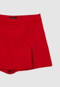 Shorts rossi strutturati con zip laterale, pieghe frontali e texture del tessuto liscia. Presentano un elastico in vita per un look aderente.