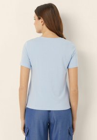 Tricou de culoare albastru deschis, cu mânecă scurtă, confecționat dintr-un material moale, cu decolteu rotund și tiv drept, purtat cu pantaloni cargo din denim.