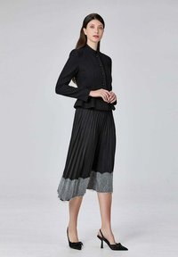 Veste noire ajustée avec des boutons, associée à une jupe plissée noire ornée d'une bordure en dentelle grise au bas. Chaussures à talons hauts noires.