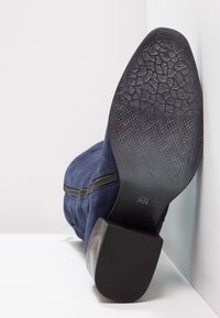 En ensam marinblå mockastövlett liggande på sin sida, som visar den texturerade svarta sulan med storleksmarkering och klack mot vit bakgrund.