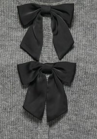 Gray knitted garment featuring two black satin bows centered at the front, each with smooth, flowing tails and a tied knot.