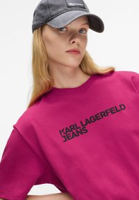 Magenta színű, oversized póló a "KARL LAGERFELD JEANS" vastag fekete betűkkel, sötét baseballsapkával párosítva. Pamut keverék anyag.