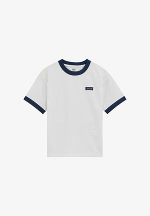 Camiseta blanca de manga corta con cuello y bordes de las mangas en azul marino, con un pequeño parche azul marino con texto blanco en el pecho izquierdo.