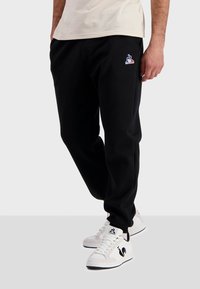 Pantalons de jogging noirs en tissu doux, avec un petit logo coloré sur la hanche gauche et des poignets élastiques à la cheville.