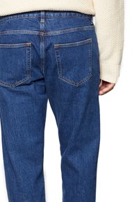 Modré džíny z denimu se střihem rovného střihu, vybavené dvěma zadními kapsami a kontrastním prošitím. Látka má hladkou, lehce vybledlou texturu.