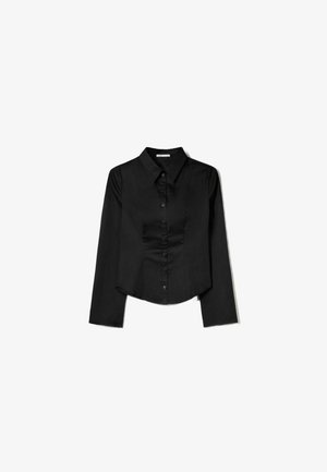 Schwarzes Langarmshirt aus glattem Stoff, mit spitzem Kragen, vorderem Knopfverschluss und einem gekürzten Saum mit seitlichen Schlitzen.
