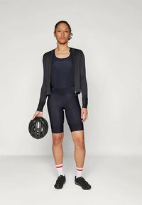 Conjunto de ciclismo preto com jaqueta com fecho de correr e calções, tecido texturizado, combinado com capacete preto e sapatilhas de ciclismo pretas, meias brancas e vermelhas.
