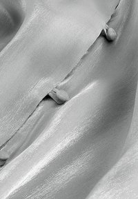 Silken gray fabric with a smooth texture, featuring small, rounded buttons along a seam. Subtle sheen enhances the material's elegance.
