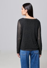 Haut à manches longues en imprimé léopard noir avec un dos transparent. Le design présente un décolleté large et une coupe ample, associé à un jean bleu taille haute.