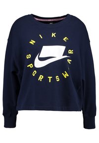 Marinblå kort sweatshirt med långa ärmar, med en stor vit Nike-logotyp och en cirkulär design med klart gula texten "SPORTSWEAR". Tillverkad av bomull.