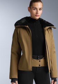 Brown jacket with a black faux fur collar, zip closure, and fitted design. Worn over a black top and belted black pants. Smooth texture.